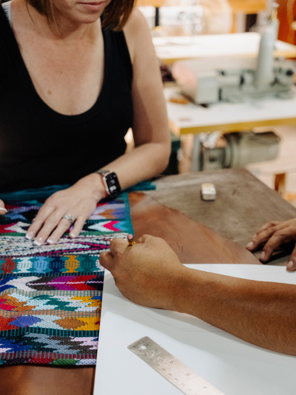 A close-up lifestyle shot of a person weaving a vibrant, multicolored geometric textile by a table with a sewing machine in the background.