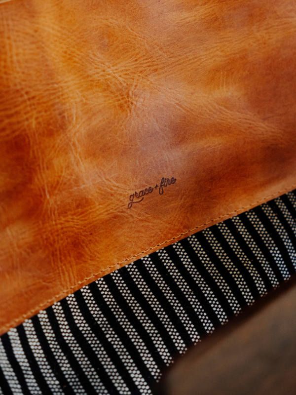 Close-up of a warm tan leather item with a small cursive 'grace fire' logo, next to a black and white striped woven textile.